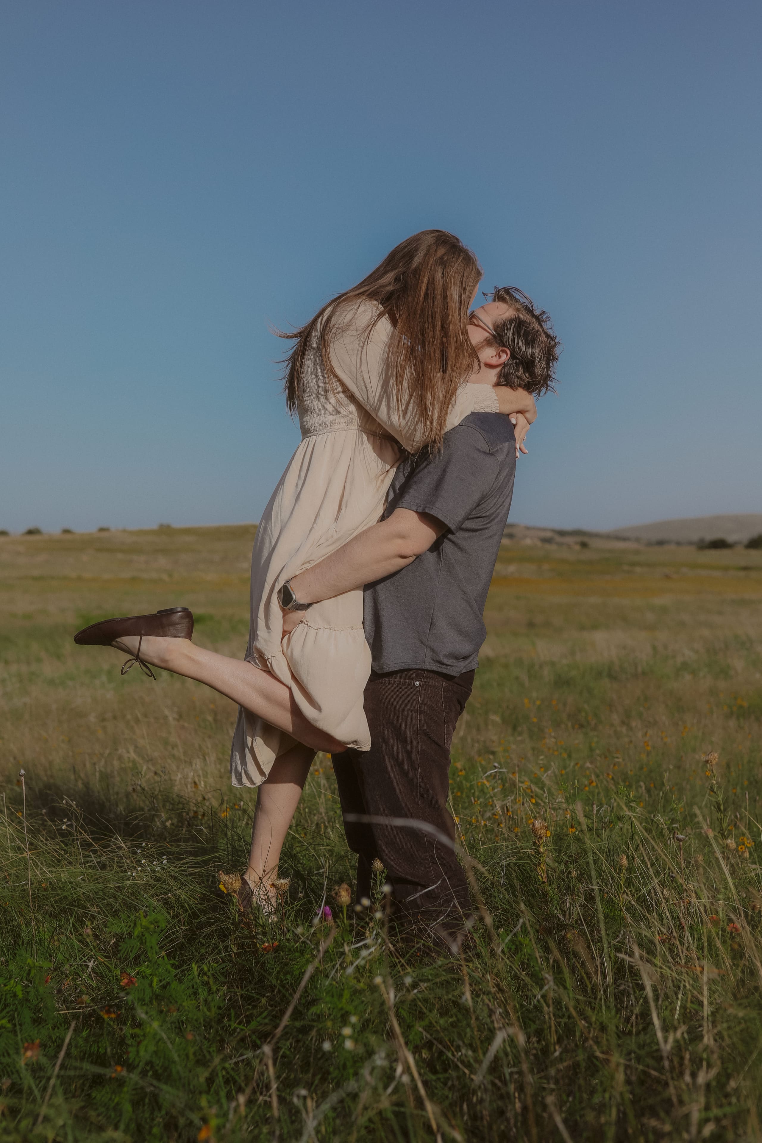 A kiss in the wildflower field, her leg kicked up mid-lift