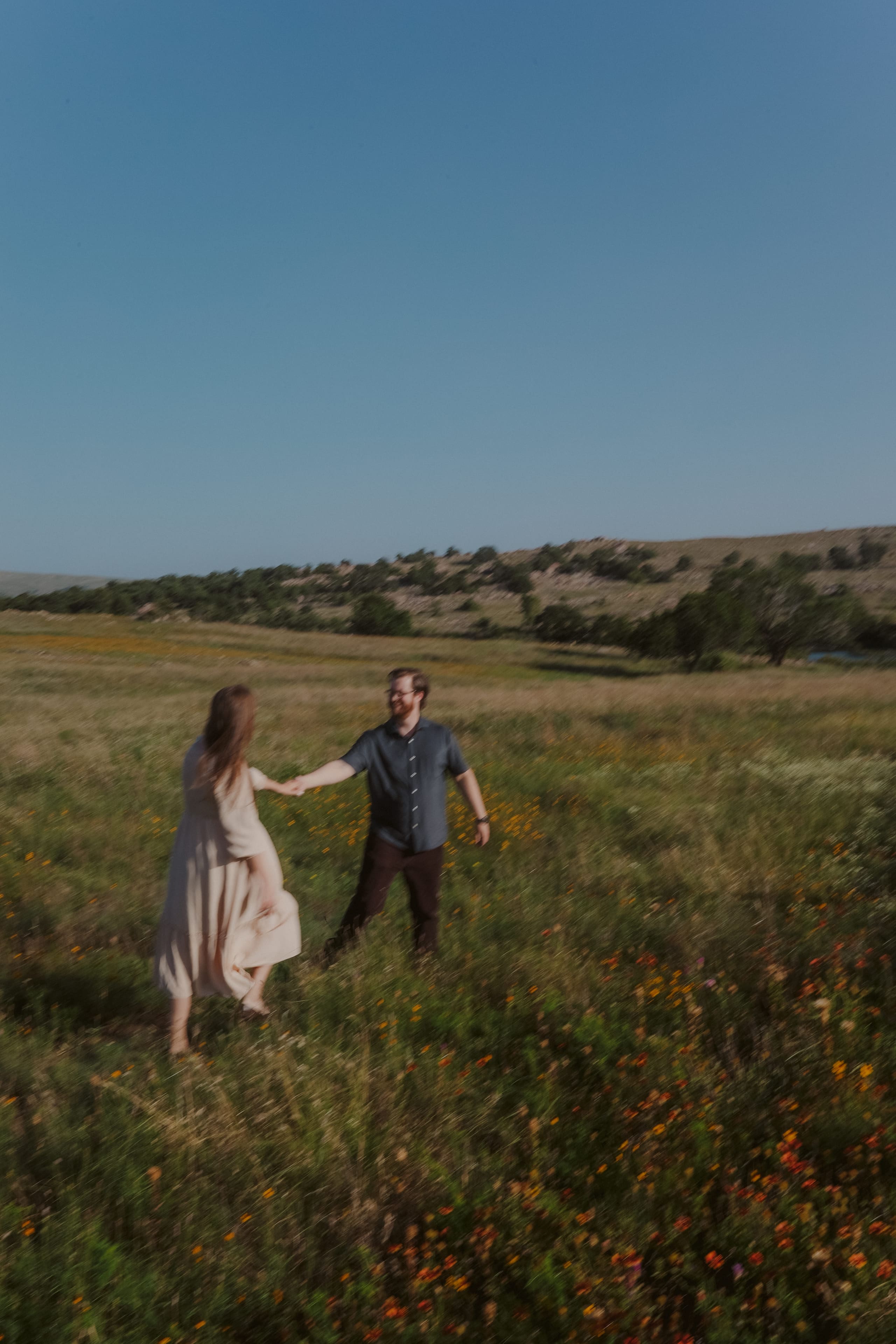 Leading him by the hand through the wildflowers, motion softly blurred