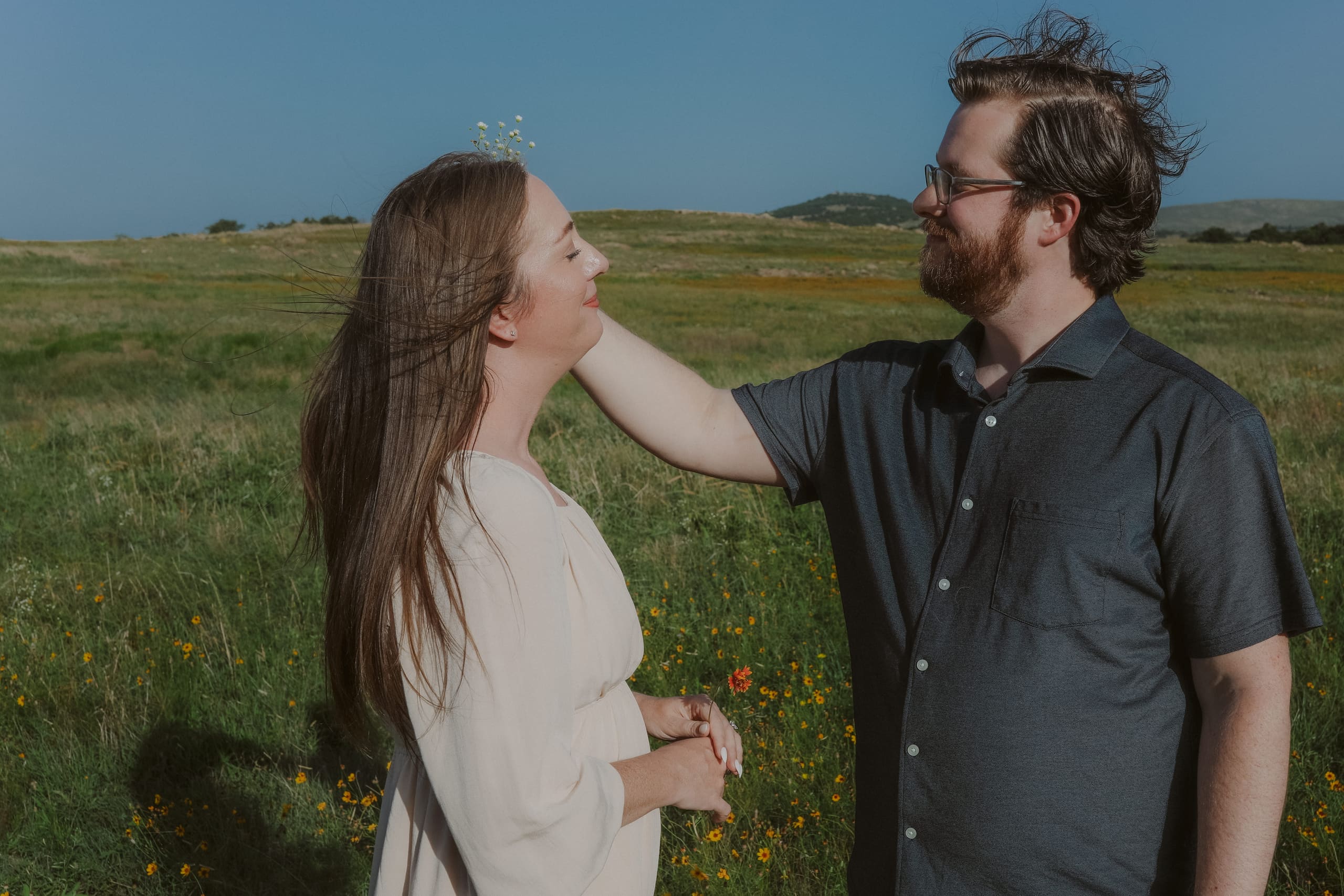 He tucks a wildflower into her hair in the sunlit field