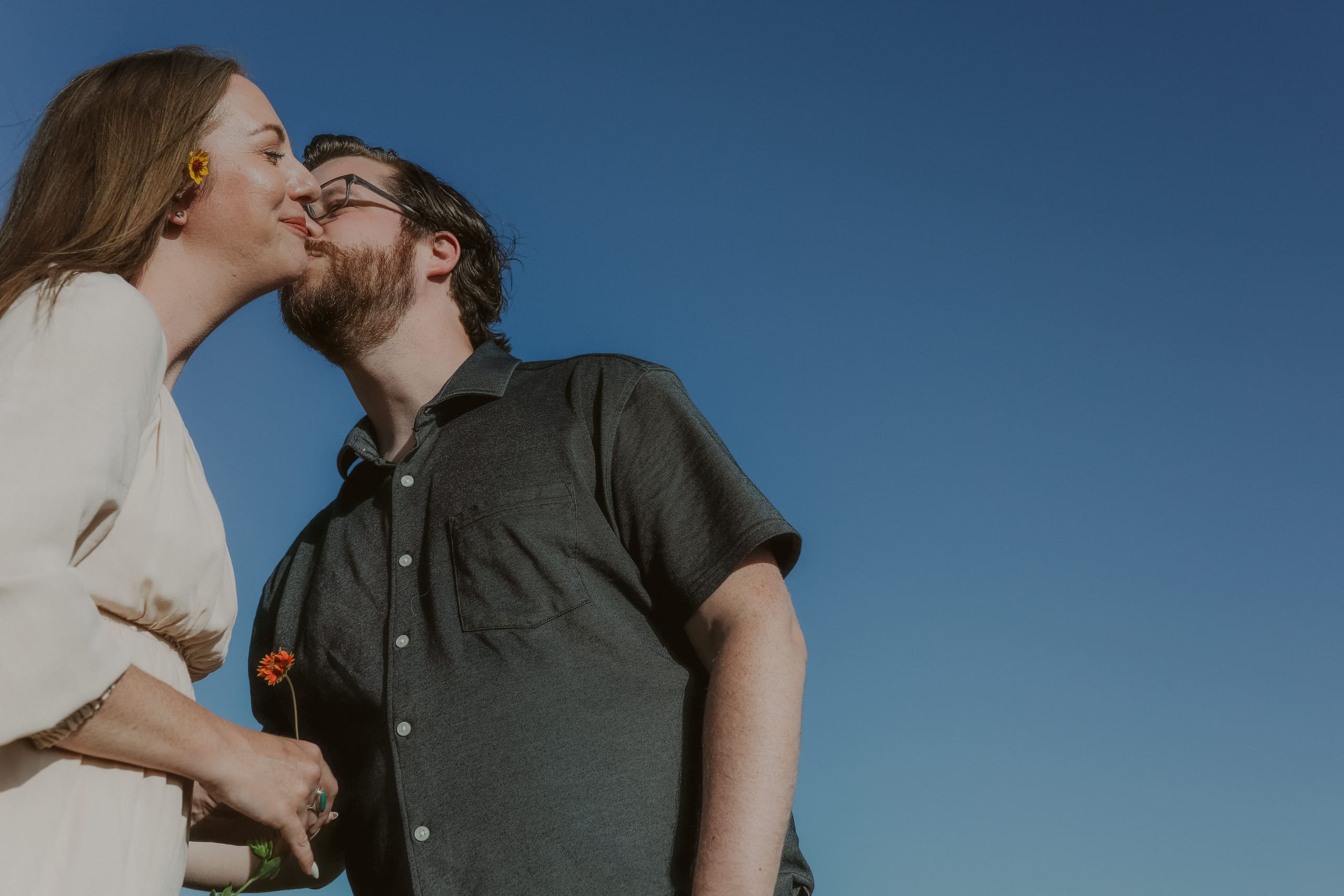 A kiss on the cheek against the open sky, flower in hand