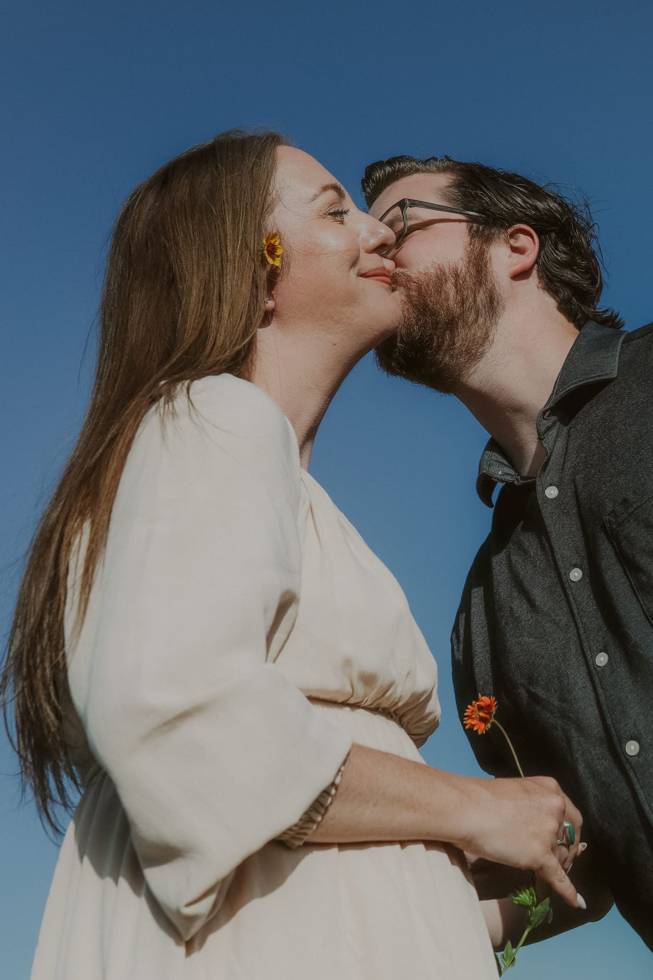 A kiss beneath the blue sky, yellow petals tucked in her hair