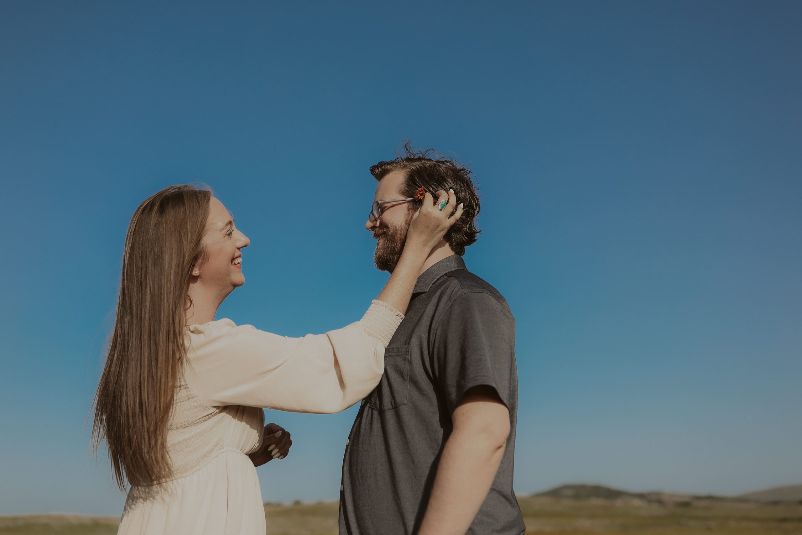 She brushes the hair from his face, both smiling in the sun