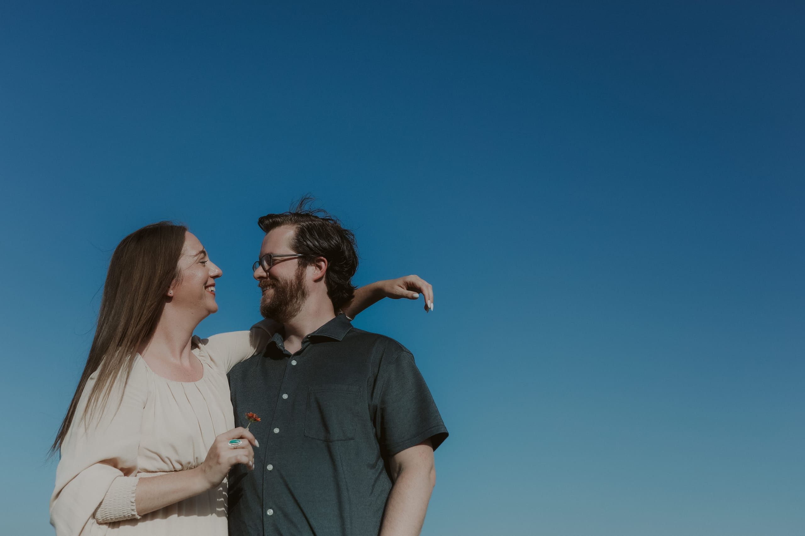 Her arm around his shoulders, laughing with a wildflower in hand