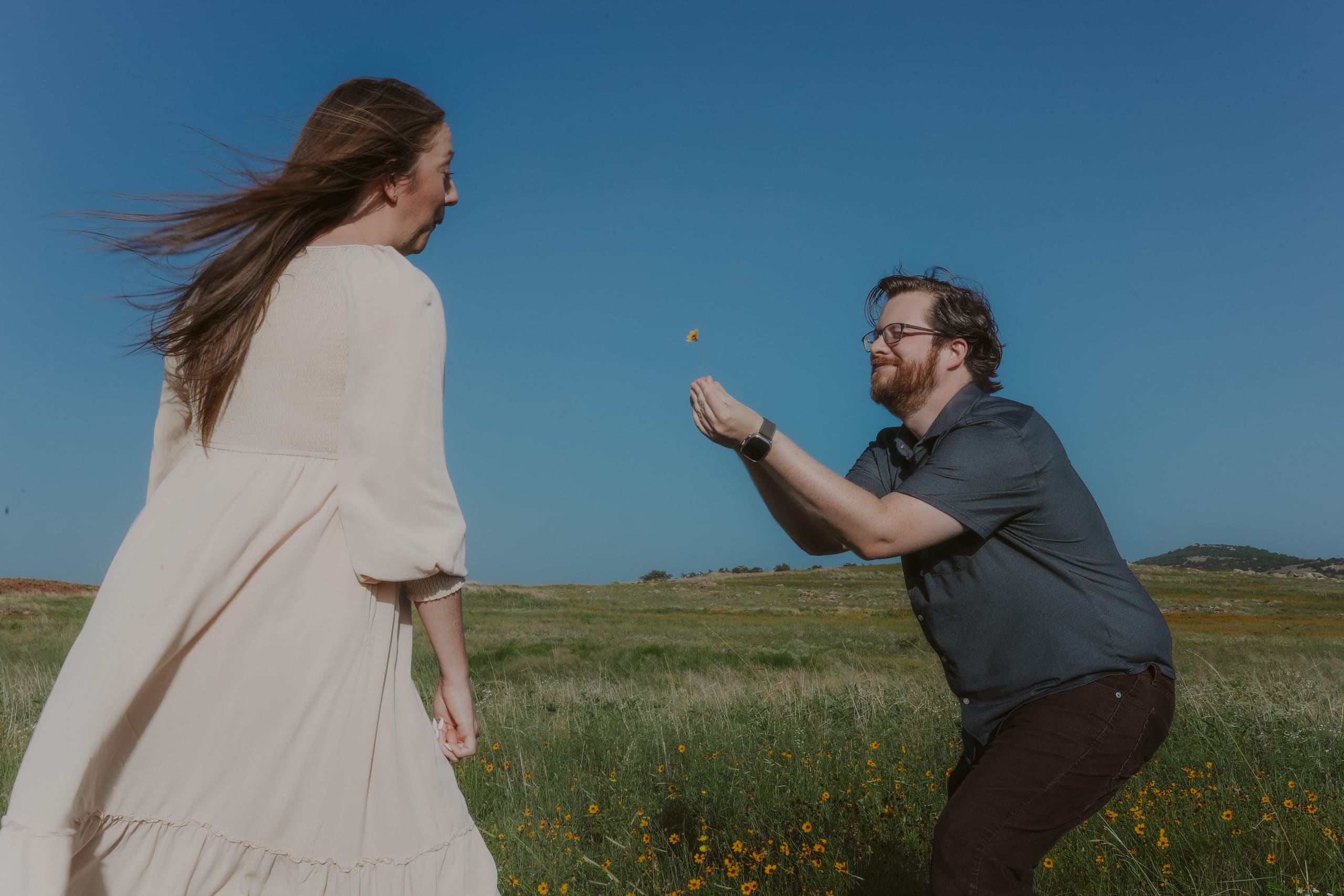 Offering her a single yellow wildflower against a wide blue sky