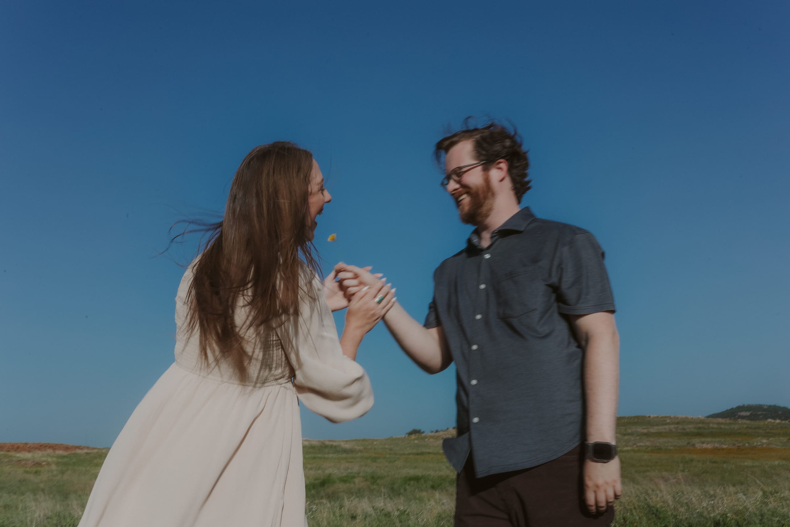 Laughing over a wildflower, hands clasped beneath a deep blue sky