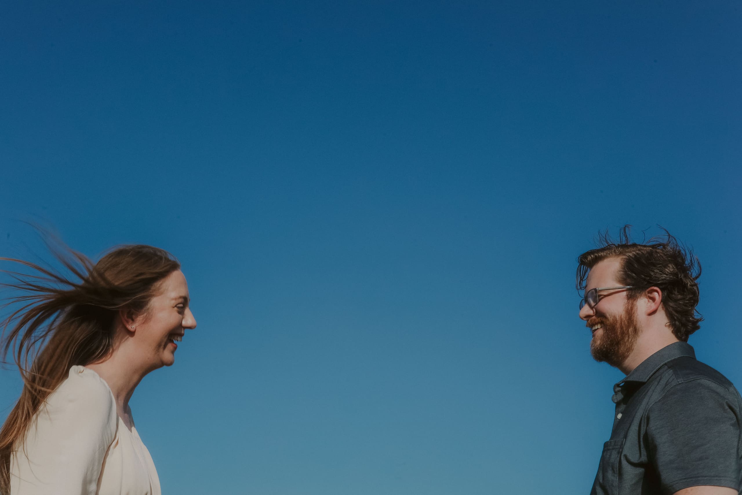 Two smiling profiles facing each other across an open stretch of blue sky