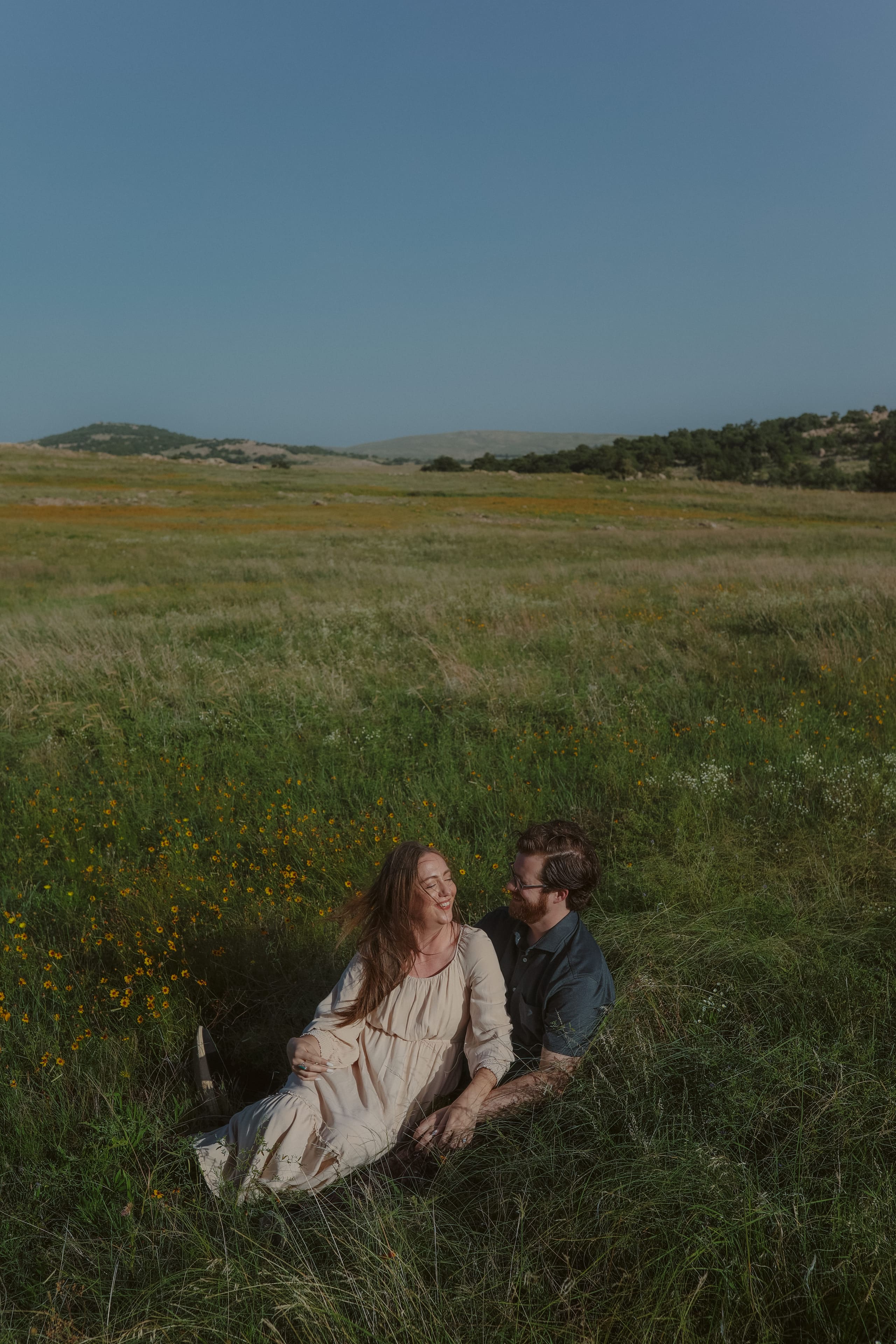 Leaning back against him in the tall grass, laughing under a wide sky