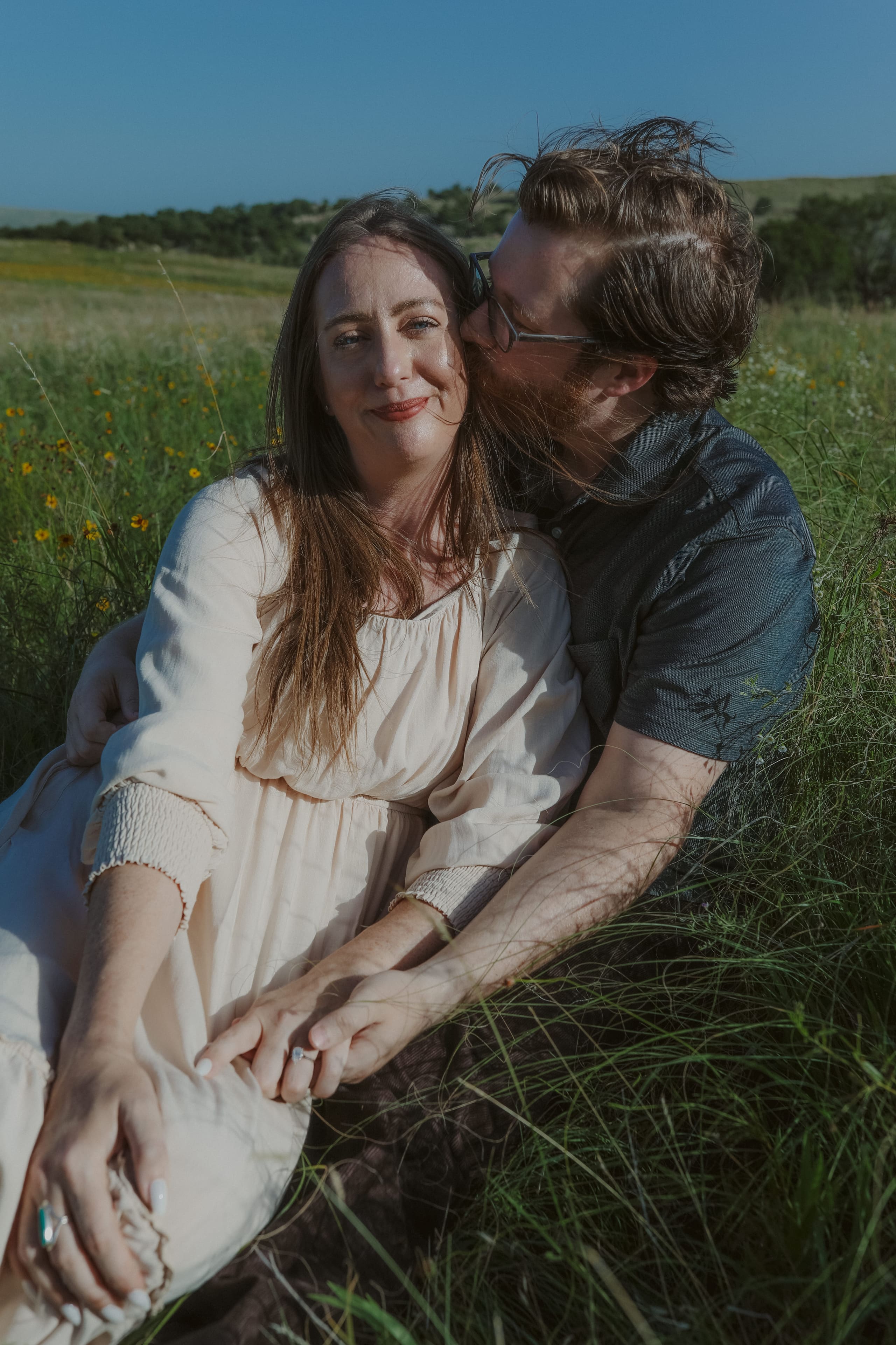 A kiss on her temple in the sunlit grass, hands intertwined