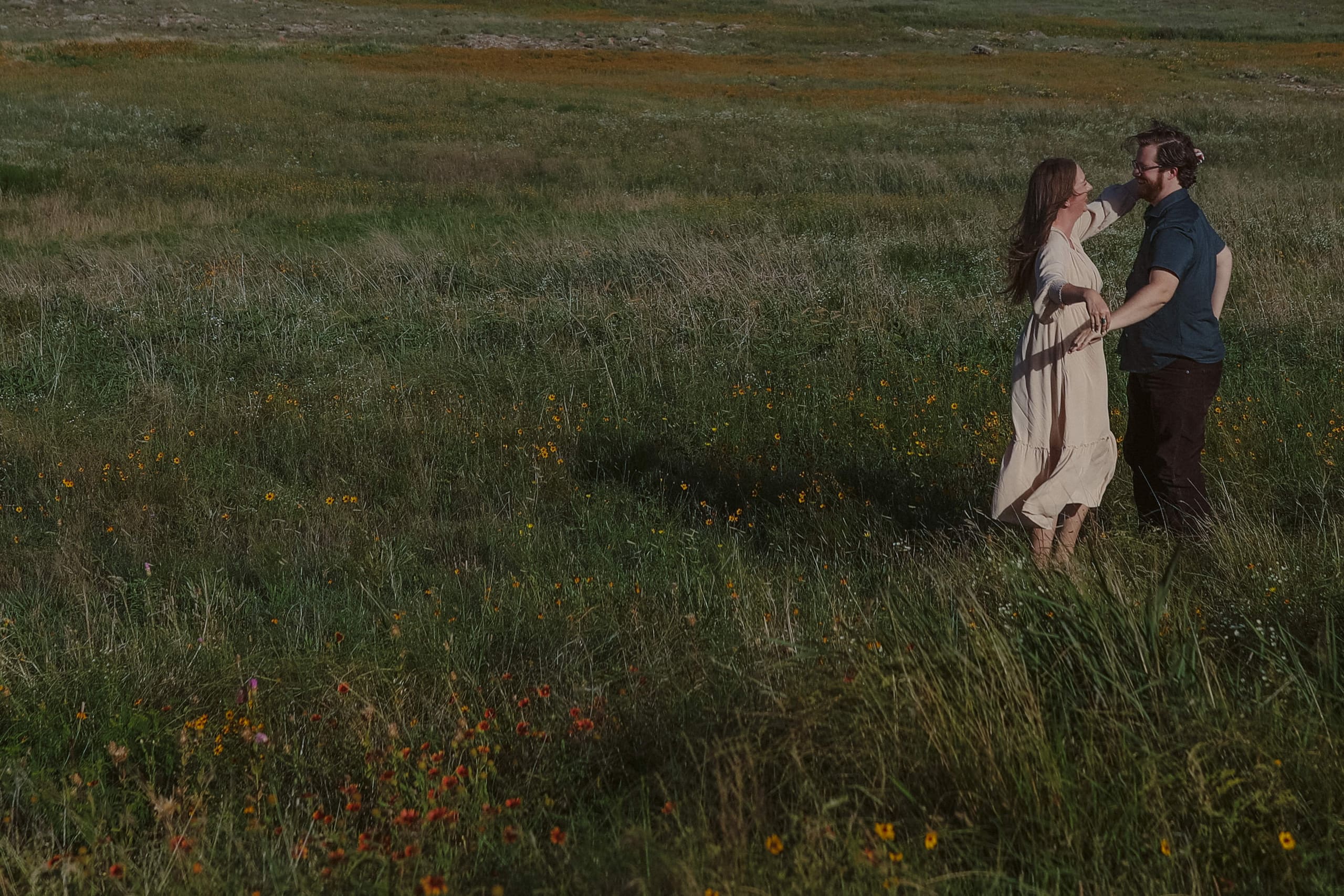 Her arm draped over his shoulder amid grass and scattered wildflowers