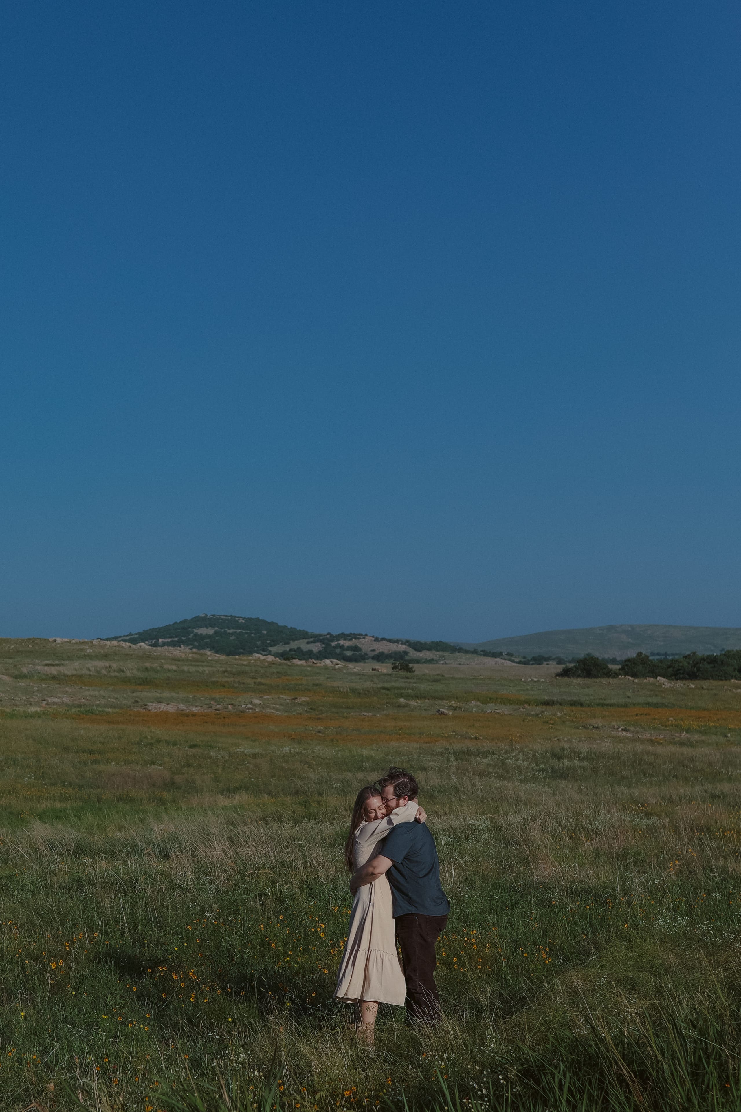 A quiet embrace beneath a towering blue sky, hills on the horizon