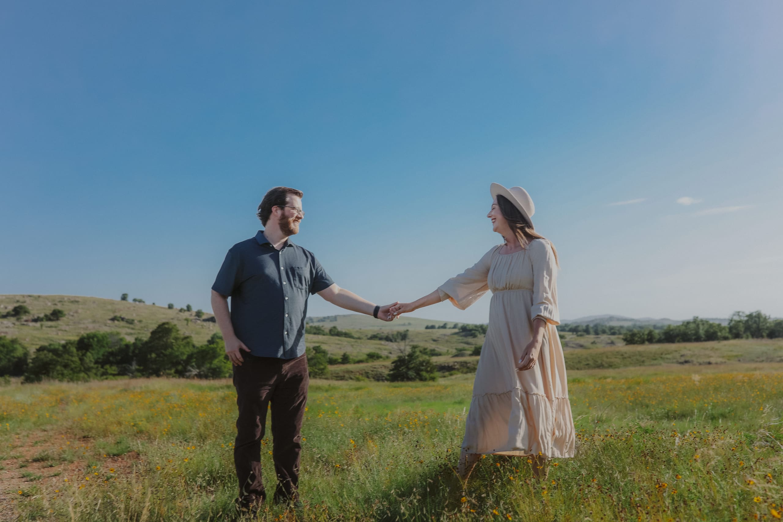 Reaching for each other’s hands in a wildflower meadow under a wide blue sky