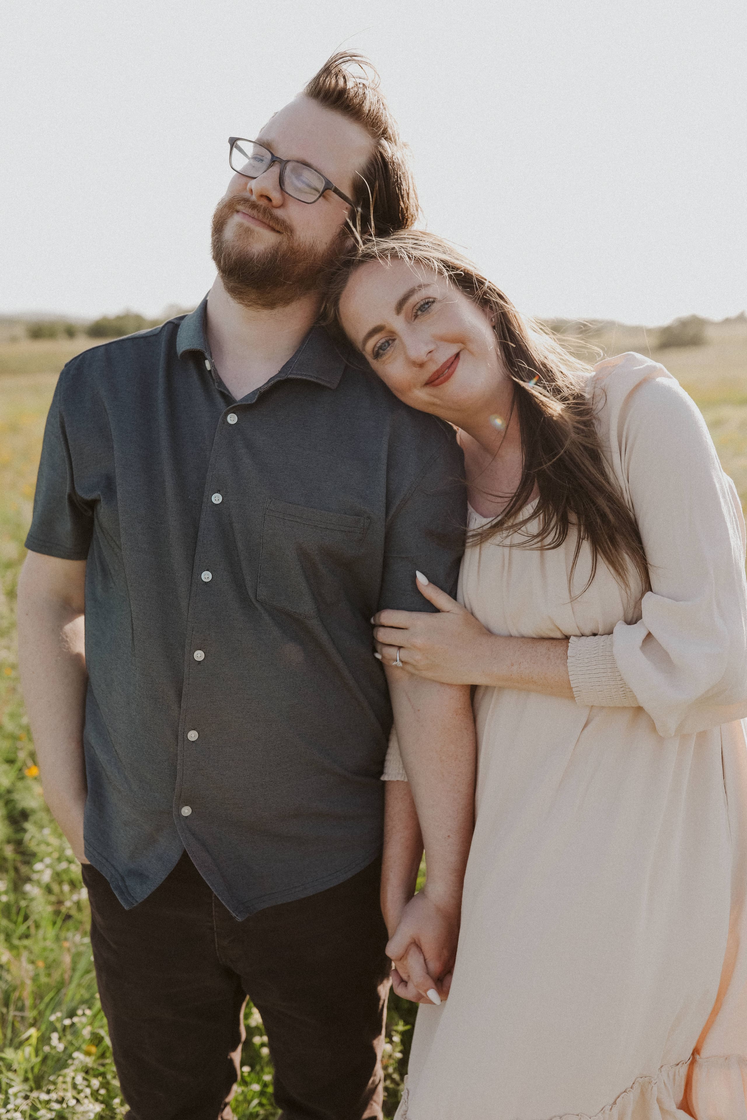 A close portrait — her cheek at his shoulder, fingers intertwined