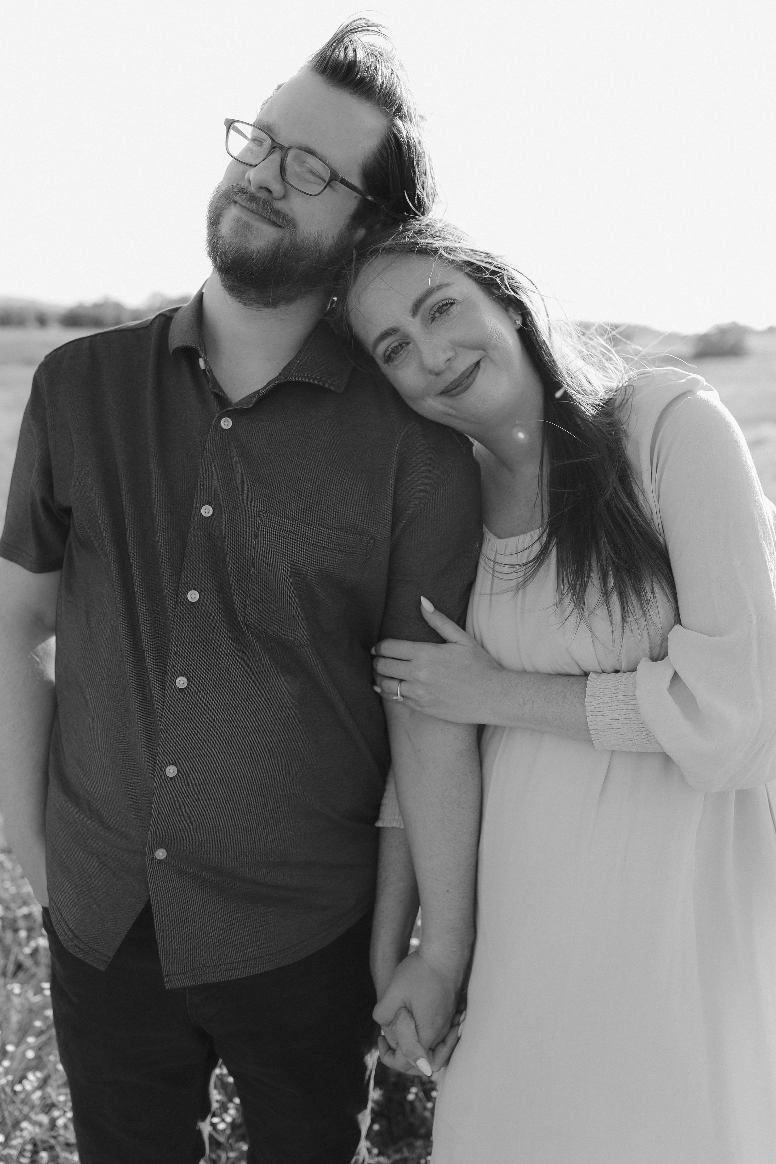 Leaning into him with a soft smile, hands joined, in black and white