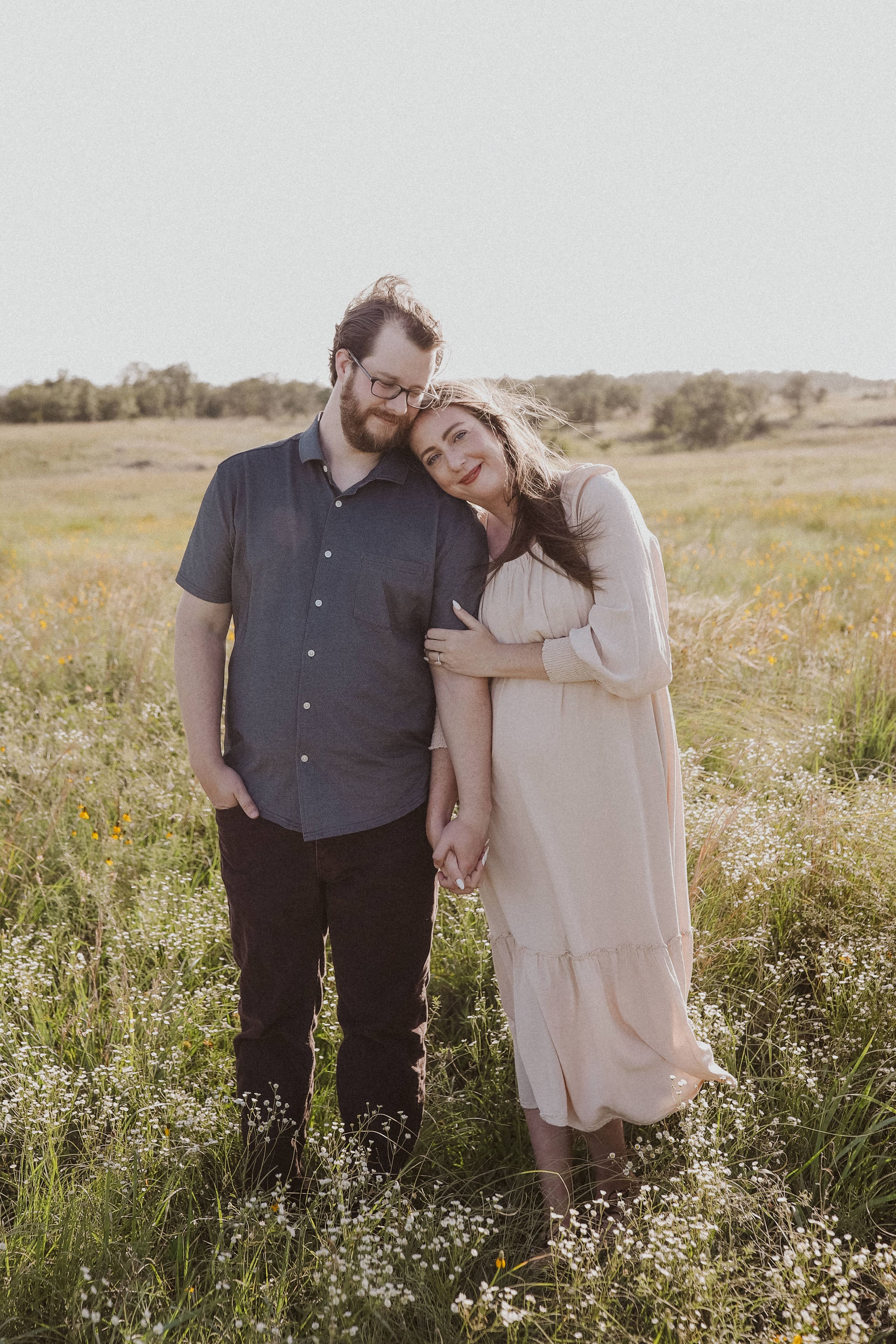 Standing close in a sea of white wildflowers, her head against his