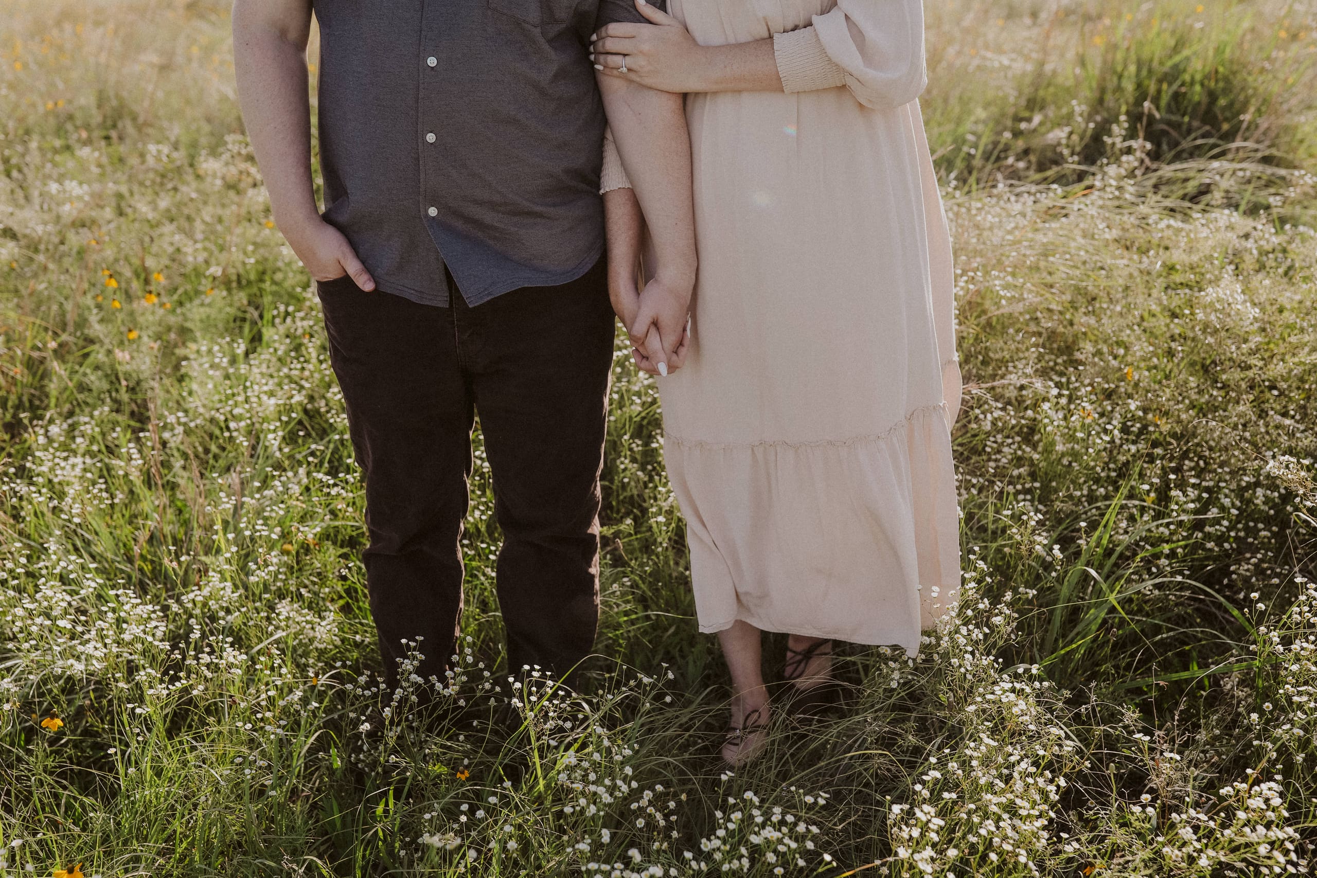 A detail of held hands between denim and blush linen in the flowers